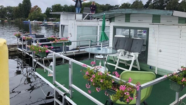 Una estructura flotante con terraza verde, asientos exteriores y plantas en macetas.