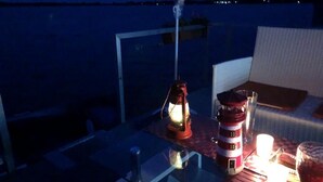 Una mesa con cubierta de vidrio, dos faroles rojos, un faro a rayas y una copa de vino.