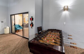 A room with a foosball table, a chair, a trash bin, and a sliding glass door leading to another room.