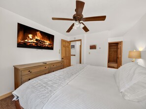 Un dormitorio con una cama, ventilador de techo, chimenea y cómoda de madera.