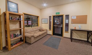 A cozy room with a beige sofa, wooden bookshelves, a glass window, an exit door, and a bulletin board.