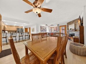 Un comedor amplio con una mesa y sillas de madera, un ventilador de techo y una cocina al fondo.