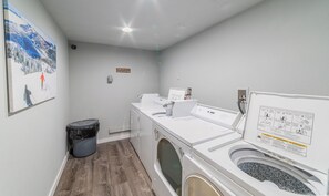 Un cuarto de lavandería con lavadora, secadora y un bote de basura.