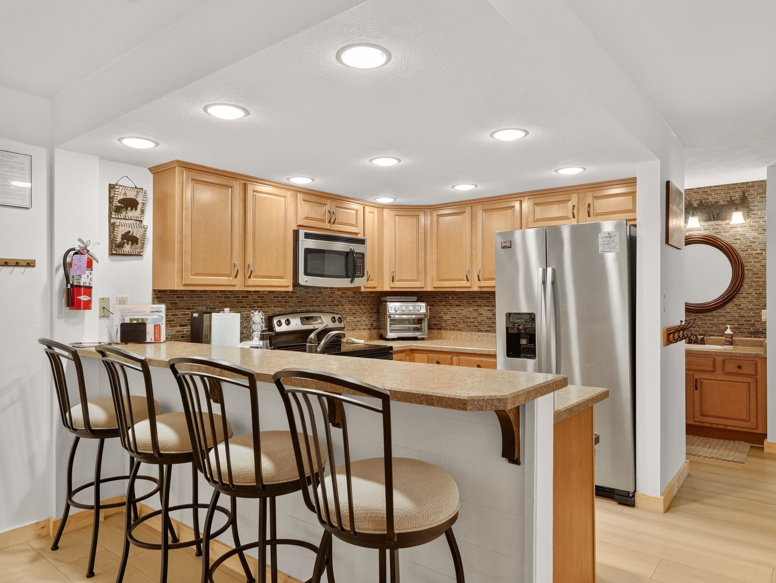 A modern kitchen with wooden cabinets, stainless steel appliances, a central island with bar stools, and recessed ceiling lighting.