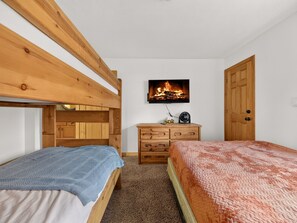 Un dormitorio con dos literas de madera, un aparador de madera, un televisor montado en la pared y una puerta.