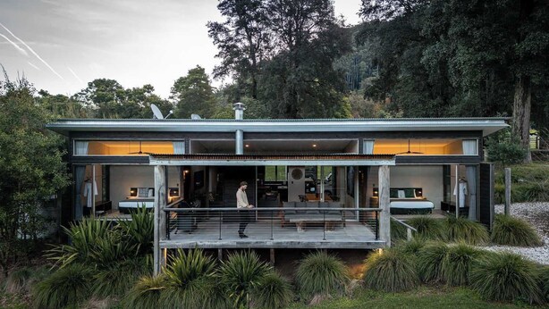 Une maison moderne à deux étages, dotée d’un balcon en verre et entourée d’une végétation luxuriante.