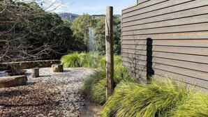 Un bâtiment en bois avec un chemin de gravier, un poteau en bois et de la végétation verdoyante.