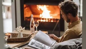 Une personne assise sur un canapé, lisant un magazine devant une cheminée.