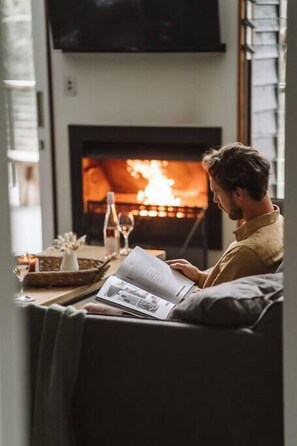 Eine Person sitzt auf einer Couch und liest eine Zeitschrift vor einem Kamin.