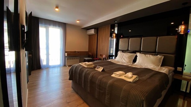 A hotel room with a large bed, a flat-screen TV, a wooden floor, and a large window. - Garden Lounge Hotel (Yerevan)
