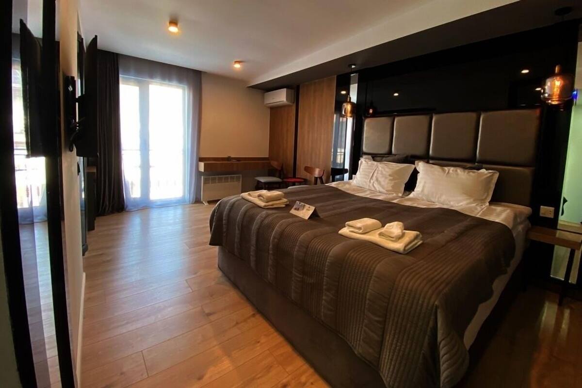 Habitación de hotel con una cama grande, un televisor de pantalla plana, piso de madera y un ventanal amplio.