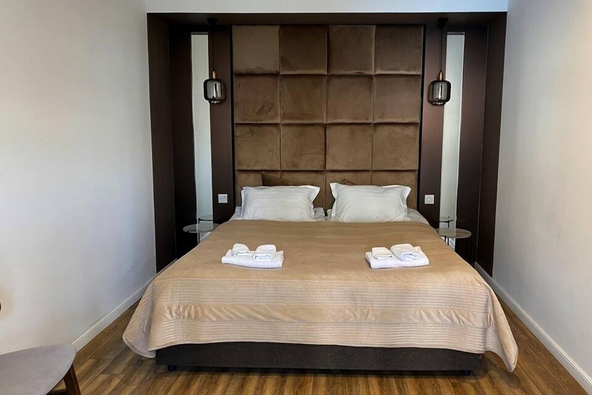 Una cama bien hecha con una colcha color beige, dos almohadas y dos toallas dobladas sobre la cama.