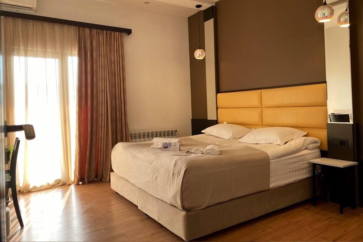 Habitación de hotel con una cama grande, una mesita de noche, una silla y una ventana con cortinas.