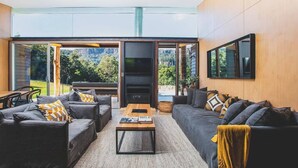 Ein modernes Wohnzimmer mit Kamin, großen Fenstern und Blick ins Freie.
