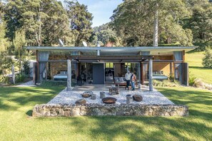 Une maison moderne dotée d’un patio couvert, d’un mur en pierre et d’une pelouse verdoyante.