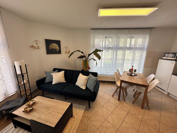 A living room with a dark sofa, a wooden coffee table, and a dining area with a wooden table and chairs. - FeWo "Goldener Steiger" für 4 Personen im Zentrum von Naumburg 99% barrierefrei (Naumburg)