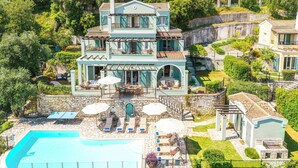 Une maison à deux étages avec une piscine, un espace salon extérieur et un mur en pierre.