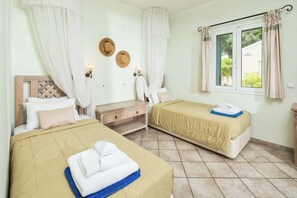Ein Hotelzimmer mit zwei Betten, einem Fenster mit Vorhängen, einem Nachttisch und einem an der Wand befestigten Haken für Hüte.