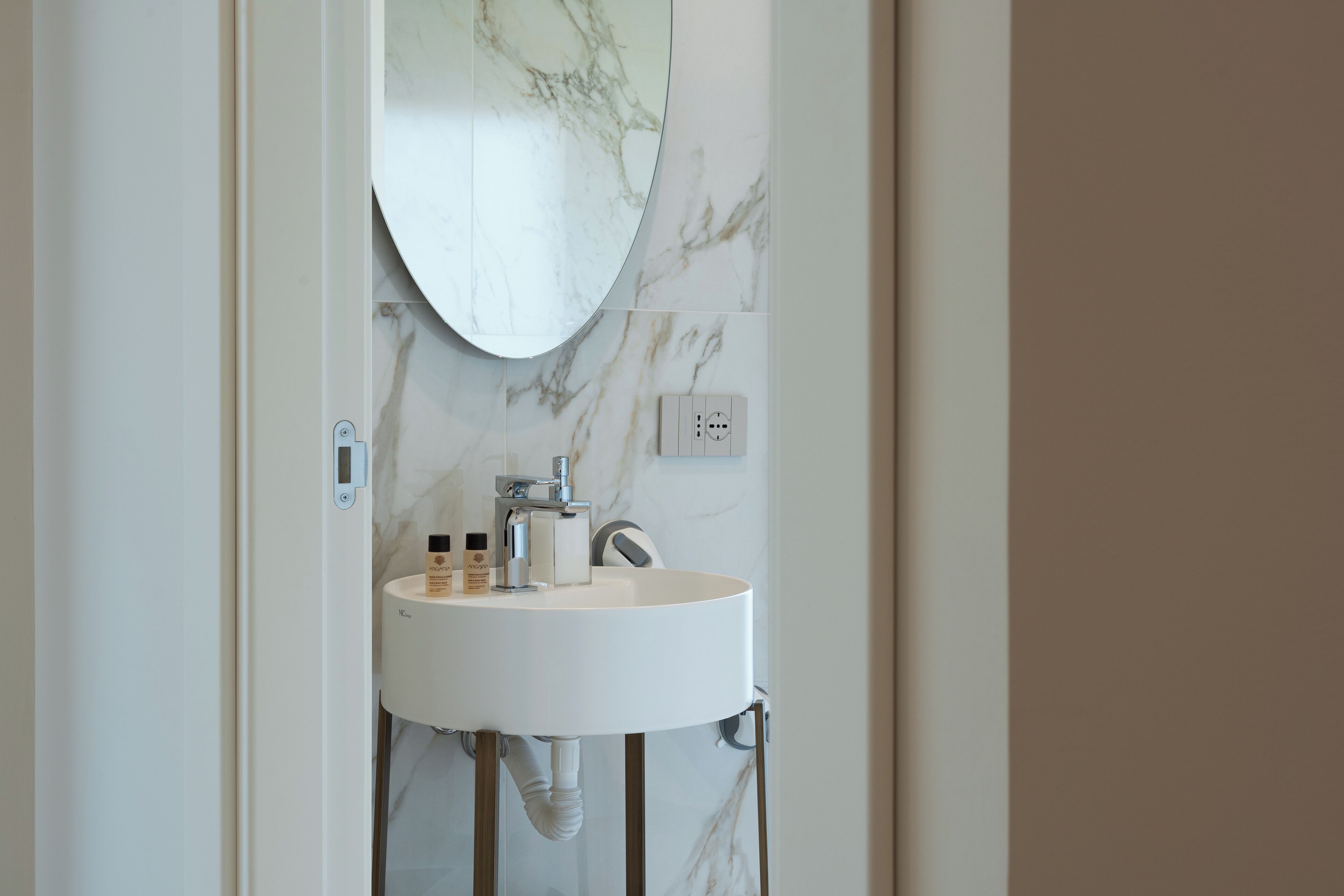 A bathroom with a white sink, a round mirror, and marble-patterned walls.