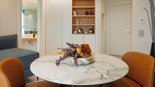 Un comedor moderno con una mesa de mármol, sillas anaranjadas, un centro de mesa decorativo y una estantería empotrada con varios objetos.