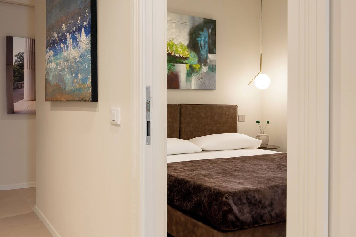 A modern bedroom with a large bed, a headboard, and two abstract paintings on the wall.