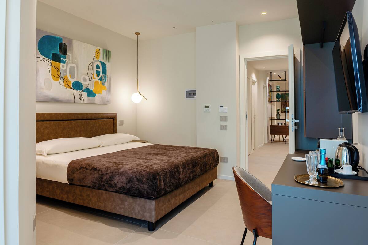 A modern hotel room with a large bed, a desk with a flat-screen TV, and a painting on the wall.