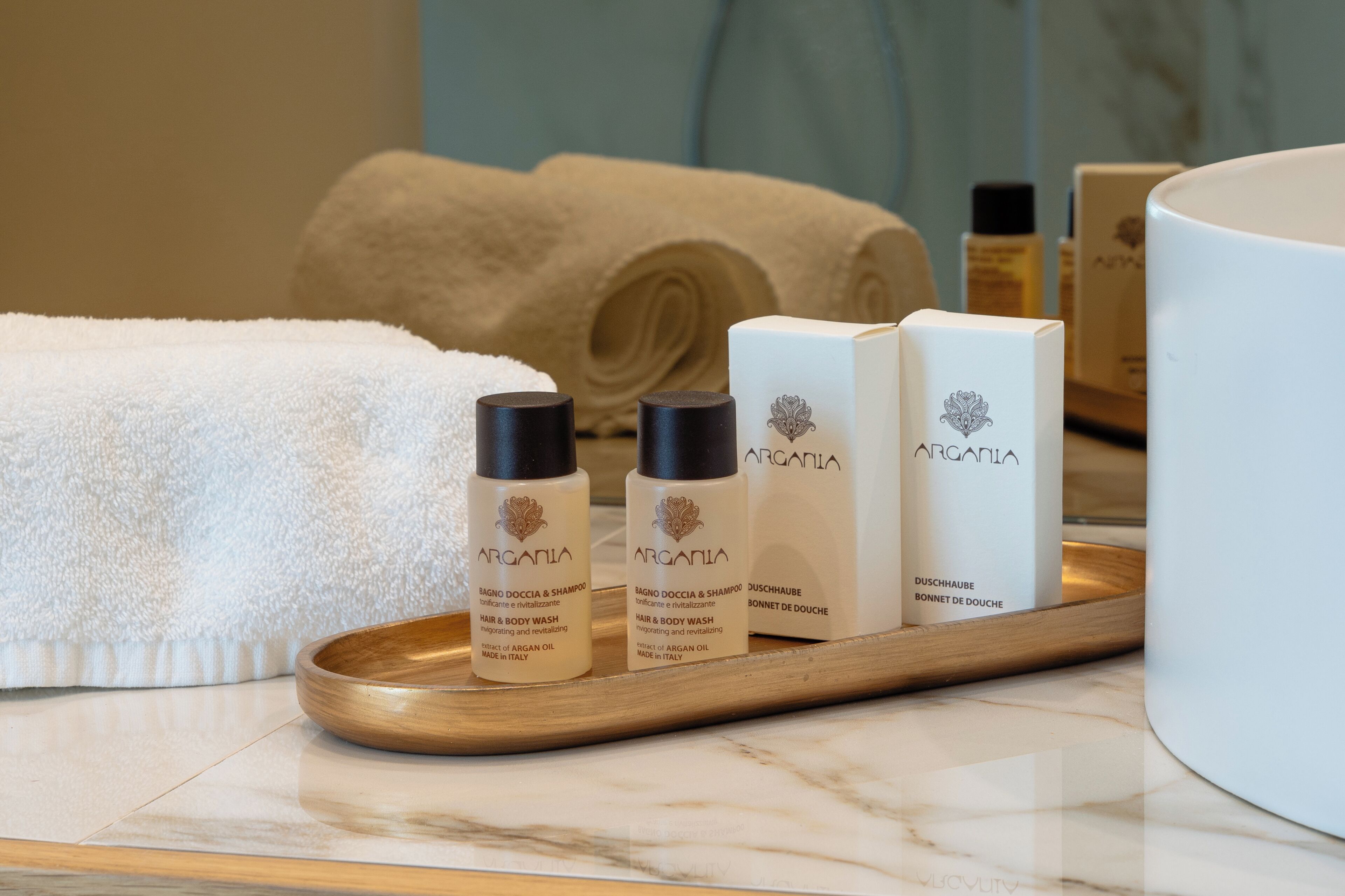 Un baño con encimera de mármol, una bandeja de madera con tres botellas de jabón para cabello y cuerpo Argania, y un lavabo blanco grande.