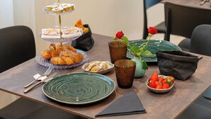 Una mesa de comedor con un expositor de postres de tres niveles, un cuenco de fresas, un florero con una rosa roja y un plato de cruasanes.