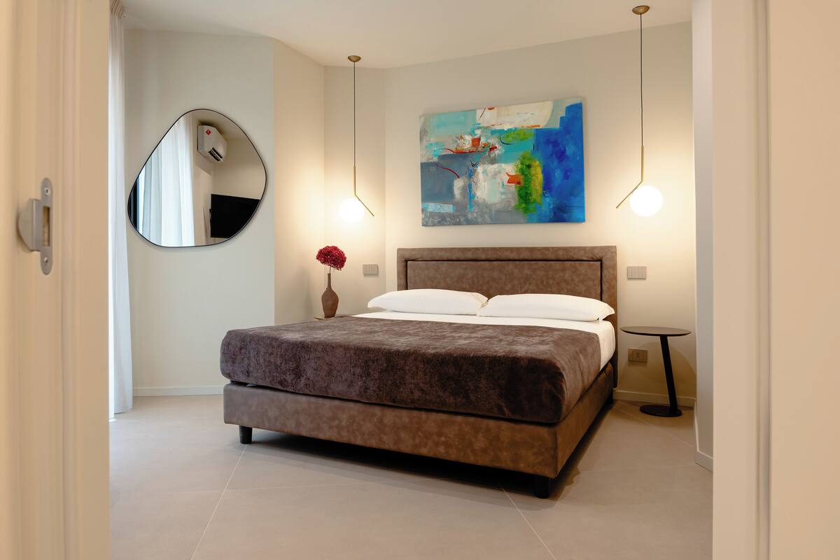 A modern bedroom with a large bed, a round mirror, a painting, and a small table.