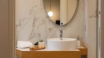A bathroom with a round white sink, a wooden vanity, a mirror, and a hanging light fixture.