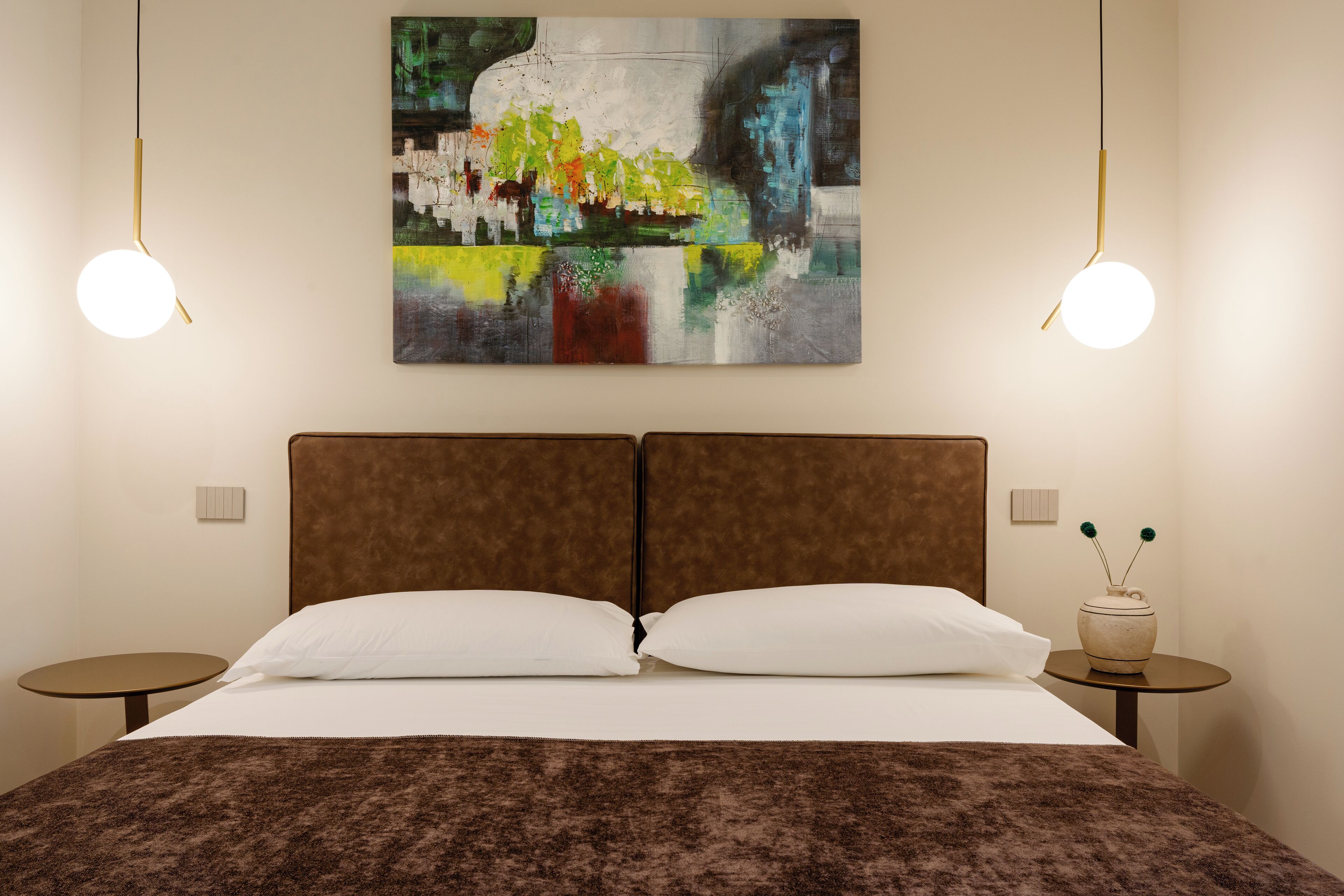 Habitación de hotel con una cama grande, dos mesitas de noche, un cuadro colgado en la pared y dos lámparas colgantes.