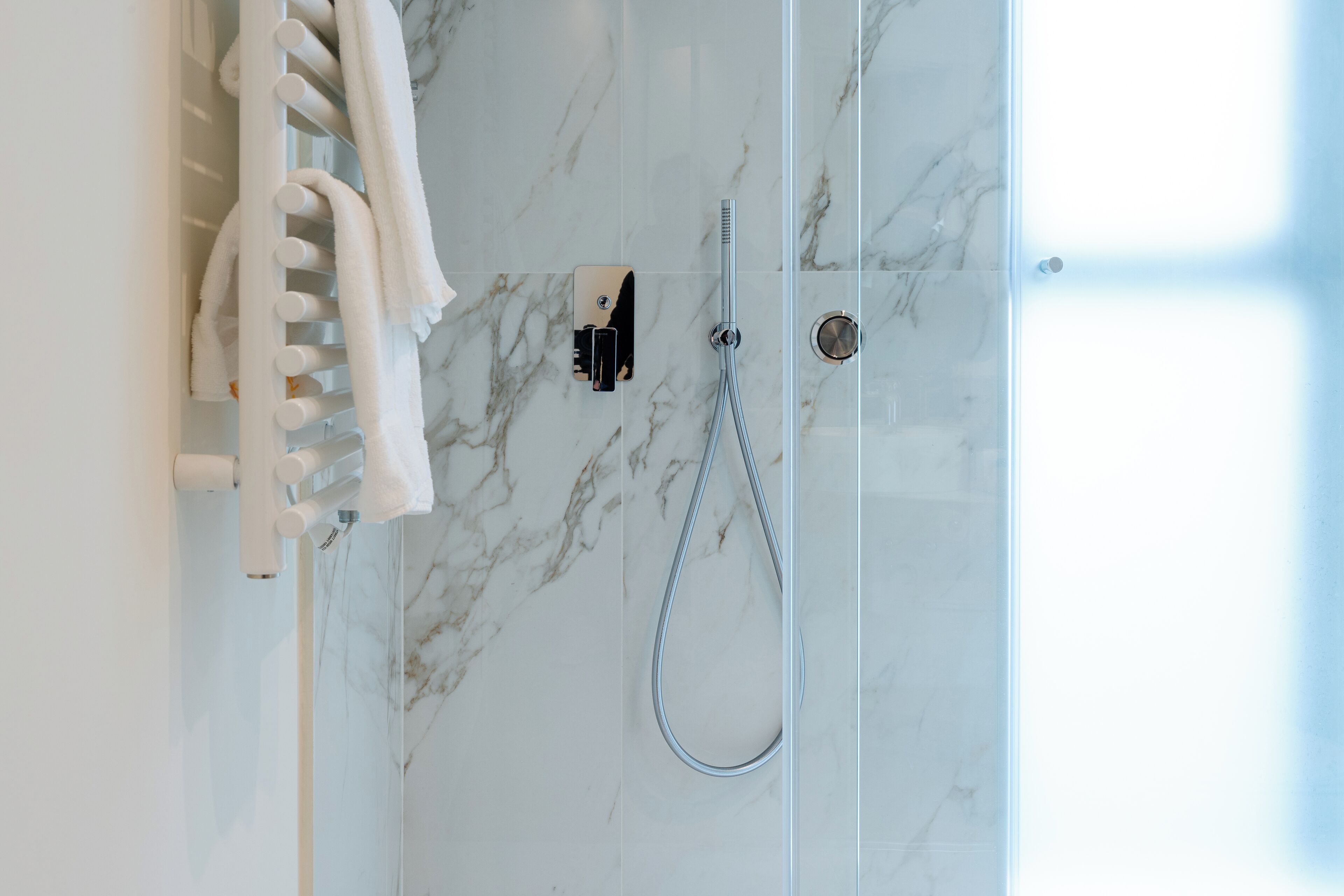 A bathroom with a glass shower enclosure, a towel rack with towels, and a control panel.