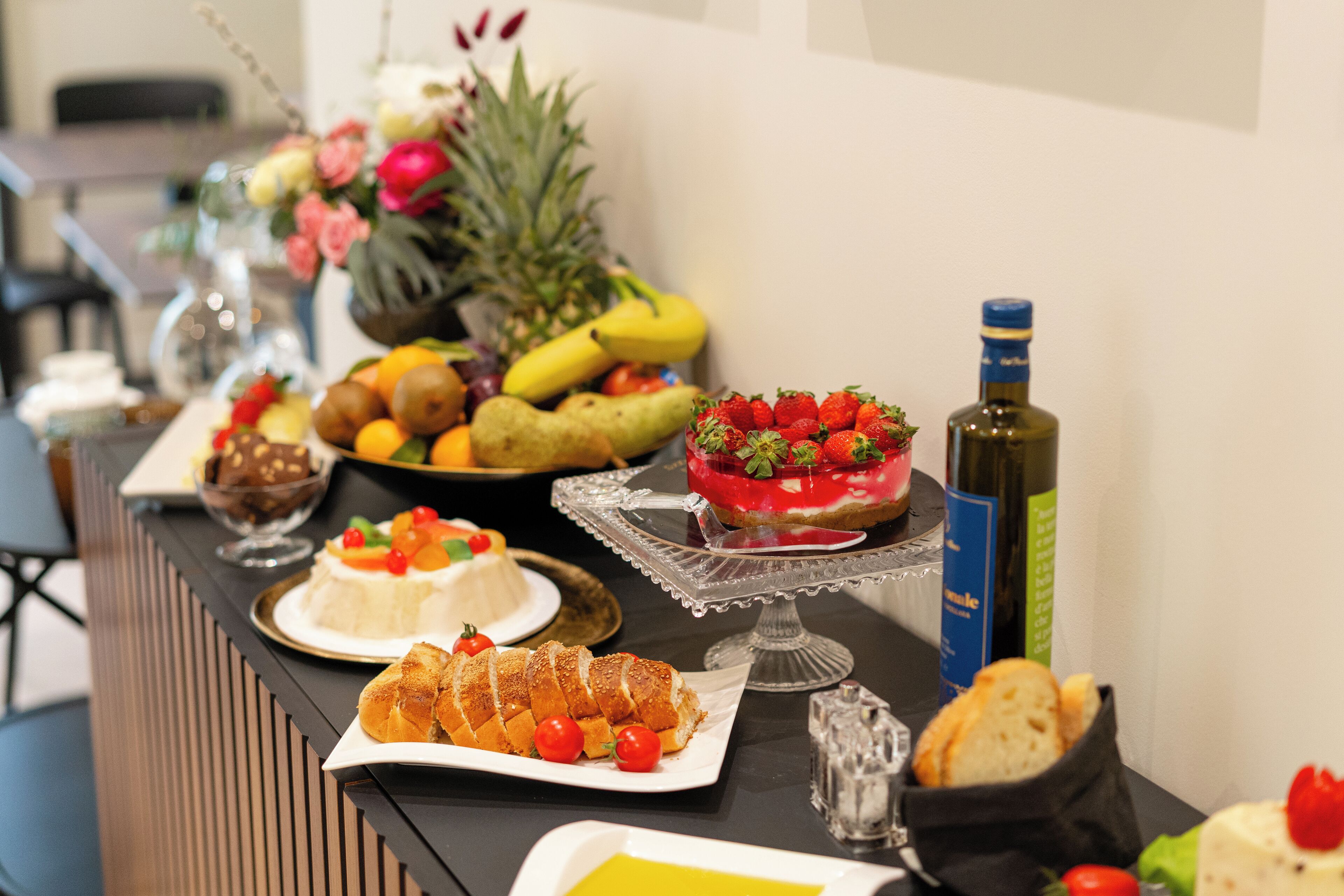 Ein reichhaltiges Buffet mit verschiedenen Speisen, darunter Obst, Gebäck und eine Flasche Olivenöl.