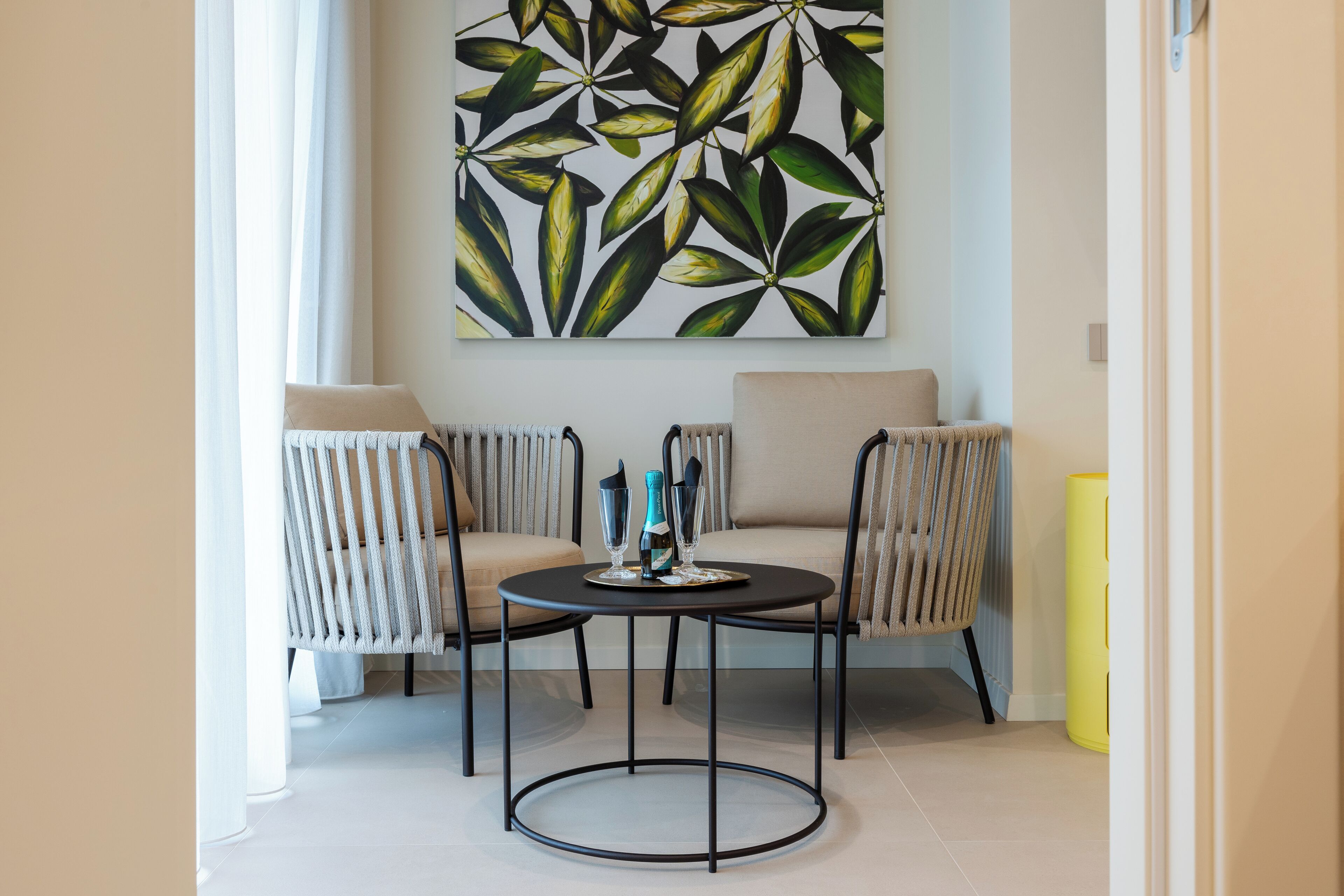 Una habitación moderna con una mesa redonda, dos sillas a rayas, un sofá color beige y un cuadro abstracto grande en la pared.