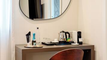Habitación de hotel con un escritorio de madera, un espejo, una cafetera, un hervidor, una botella de champán y una taza.