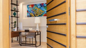 Un espacio de oficina moderno con un escritorio, una silla y estanterías. Hay un cuadro abstracto y colorido en la pared y una lámpara blanca sobre el escritorio.