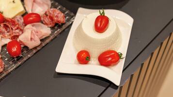 Une assiette blanche sur laquelle repose un plat en forme de dôme, agrémenté de tomates cerises et d’une feuille verte, le tout posé sur un plan de travail noir.