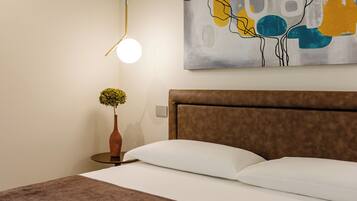 A neatly made bed with a brown headboard, a round table with a vase of flowers, and a modern abstract painting on the wall.