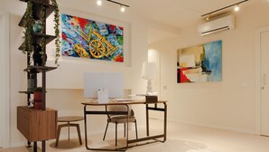 Un espacio de oficina moderno con un escritorio de madera, dos sillas, una planta en maceta y pinturas abstractas en las paredes.