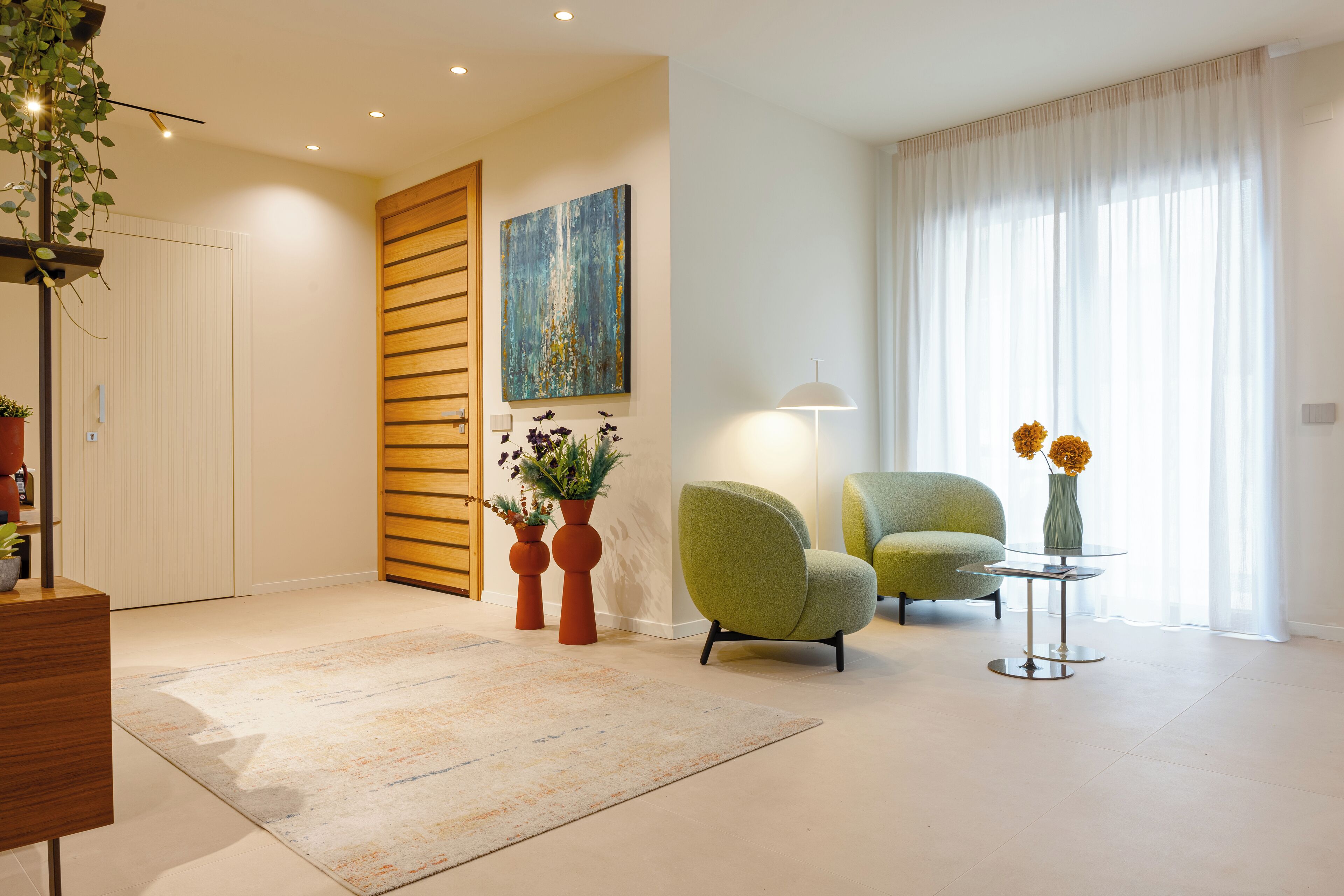 Een moderne woonkamer met een groene fauteuil, een klein rond tafeltje met een vaas, en een schilderij aan de muur.