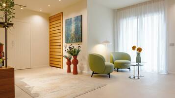 Een moderne woonkamer met een groene fauteuil, een klein rond tafeltje met een vaas, en een schilderij aan de muur.