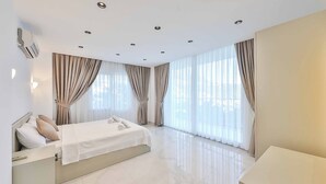 A modern hotel room with a large bed, a bedside table, and a large window with curtains.