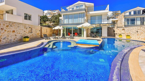 A modern pool area with a clear blue pool, lounge chairs, and umbrellas.