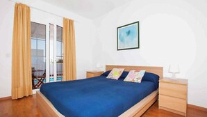 A bedroom with a large bed, wooden nightstands, a sliding glass door to a balcony, and a framed picture on the wall. - Villa Dolores - Three Bedroom Villa, Sleeps 6 (Puerto del Carmen)