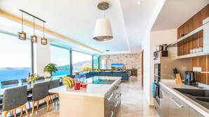 Une cuisine moderne dotée d’un îlot central, d’appareils électroménagers intégrés et offrant une vue sur la mer.
