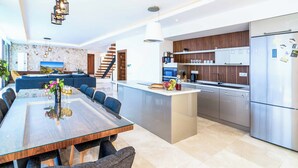 Une cuisine moderne dotée d’un îlot central, d’appareils électroménagers en acier inoxydable et d’un coin repas avec une table et des chaises en verre.