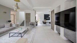 A modern living room with a sofa, coffee table, and TV. There is a staircase leading to another room.