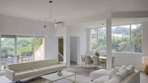 A spacious living area with a white sofa, a coffee table, and a dining area with chairs.