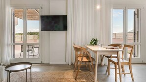 Un comedor con una mesa, sillas, un televisor y vistas amplias a través de grandes ventanales.