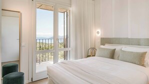 Un dormitorio con una cama grande, vistas a un balcón por una puerta corrediza y una mesita de noche con lámpara.